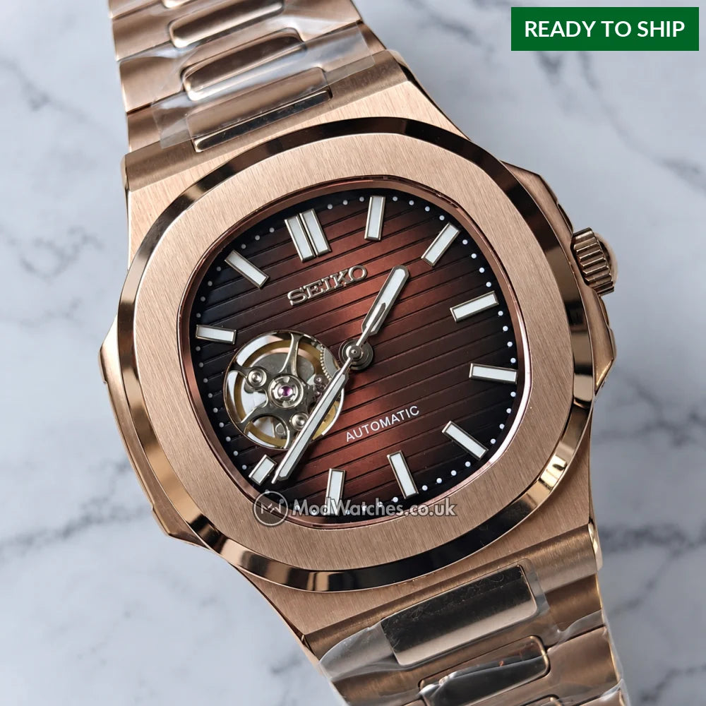 A Seiko Mod watch with a brushed rose gold-tone metal case and bracelet, featuring a dark brown sunburst dial with a visible mechanical movement through an open window.